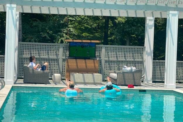 Outdoor TV lift cabinet by pool and pergola